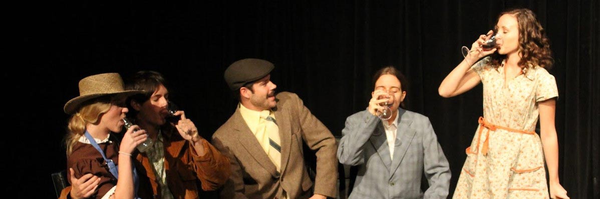 Five students in vintage costume drink wine on stage
