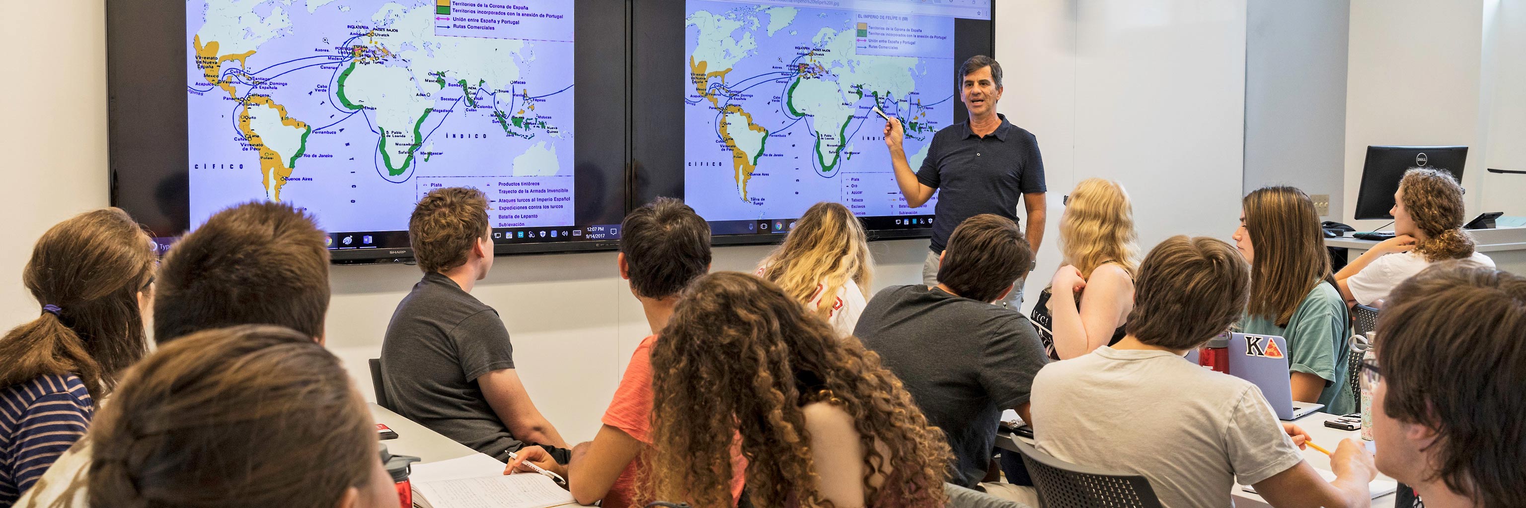 Instructor lectures in front of a world map to a class of students 