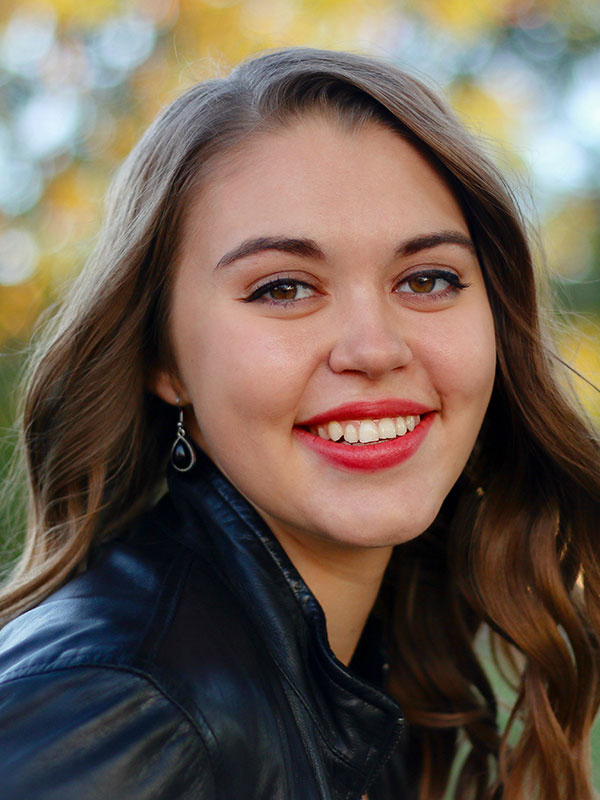 A headshot of Abby DeArmitt, who wears a leather jacket and poses outside.