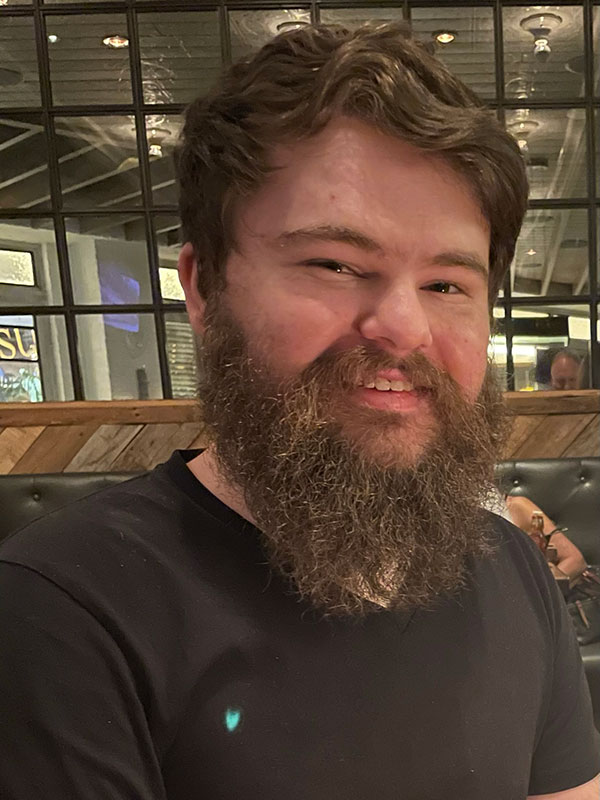 A headshot of Abe Kassis, who wears a black shirt and poses in a restaurant.