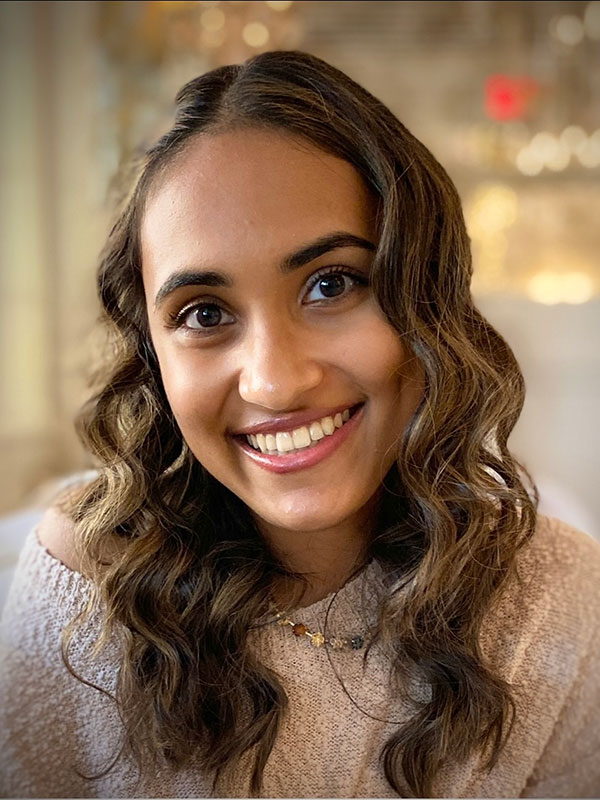 A headshot of Amee Punater, who wears a beige sweater and poses against a blurry, golden background.