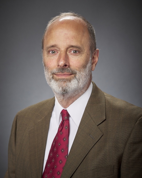 A headshot of Galen Brokaw, who wears a tan suit and a dark red tie.
