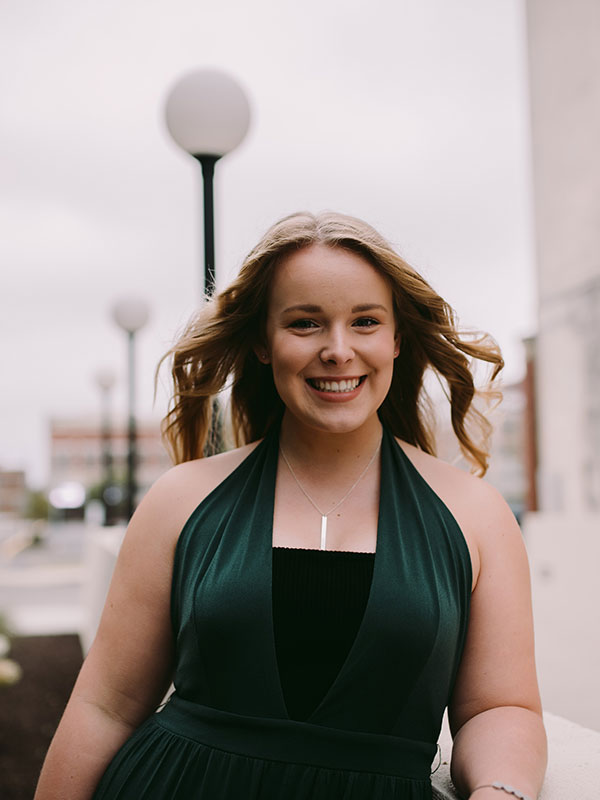 A headshot of Kaitlin Scott, who wears a green dress and poses outside.