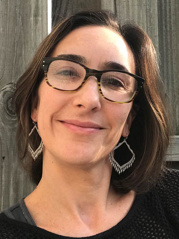 A headshot of Gaëlle Le Calvez House, who wears a dark shirt and poses against a wooden fence.