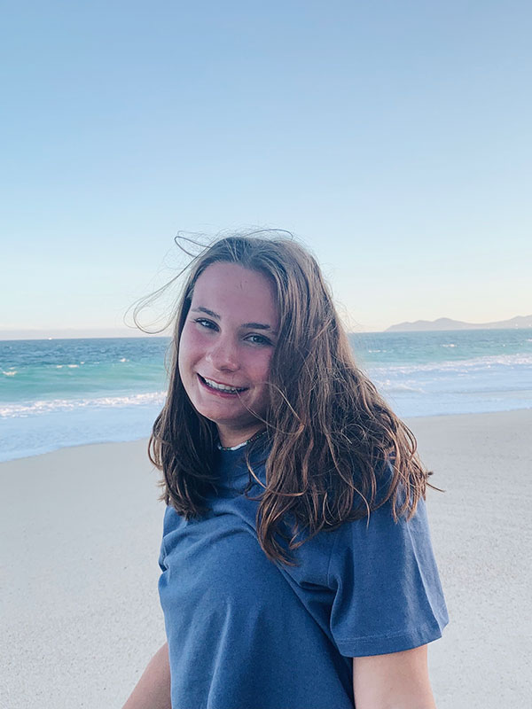 A headshot of Margaret Robinson, who wears a blue shirt and poses on a beach.