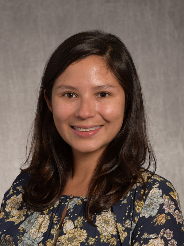 A headshot of Cynthia Martinez, who wears a floral-print shirt and poses against a beige background.