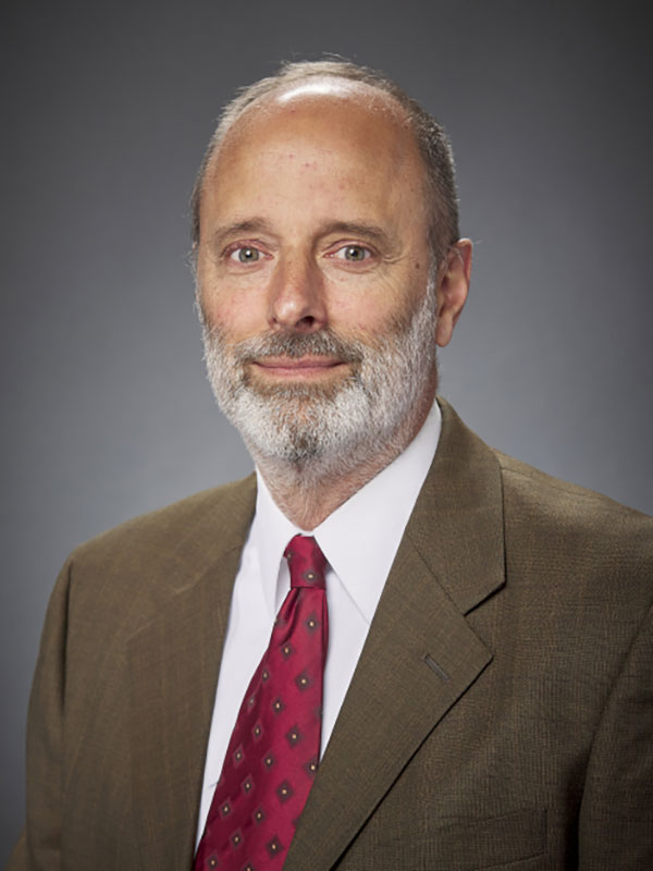 A headshot of Galen Brokaw, who wears a tan suit and a dark red tie.