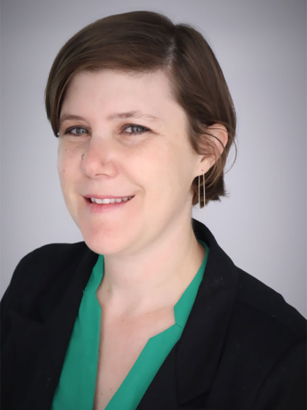 A headshot of Cara Kinnally, who wears a black blazer and green dress shirt.