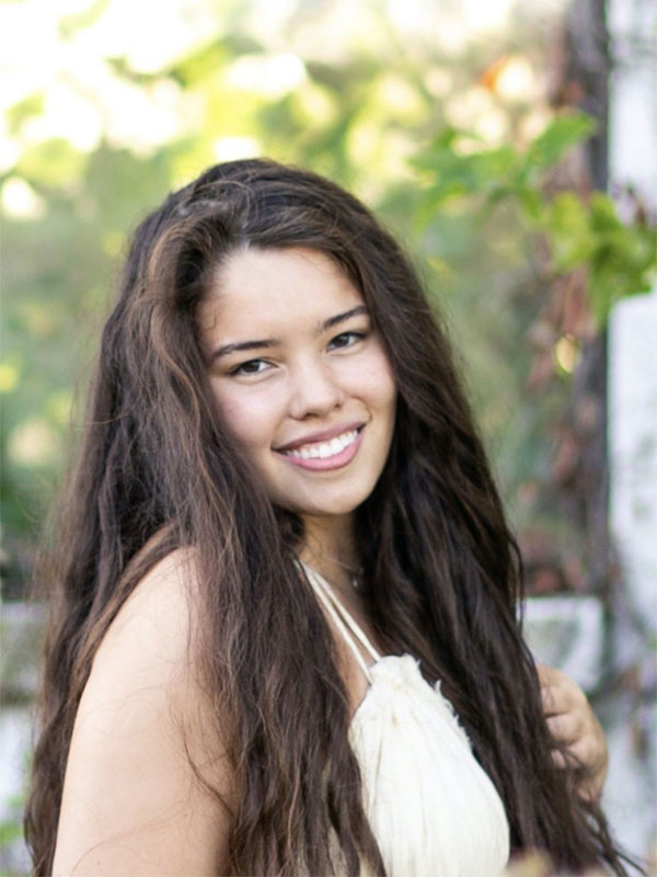 A headshot of Ginelle Suico, who wears a white shirt and poses outdoors.