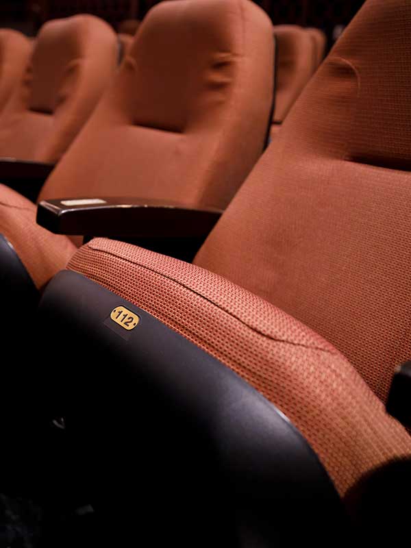 An empty row of red fabric seats in a theatre.