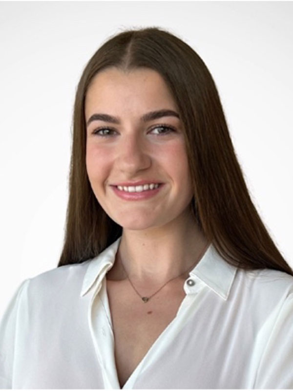Portrait of a person with long straight hair wearing a white blouse, smiling against a light background.