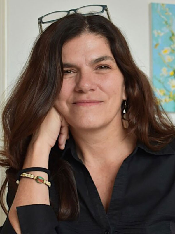 Portrait of a person with long brown hair wearing a black shirt, resting their head on one hand and smiling gently.
