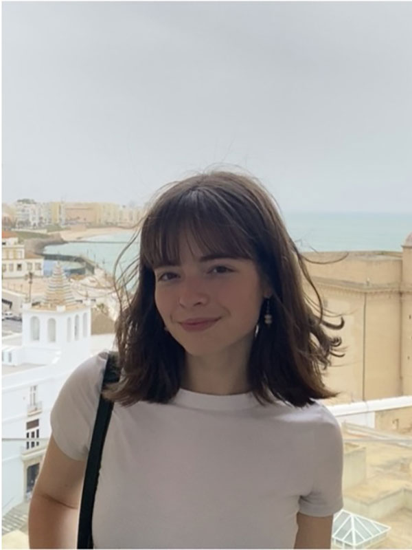 Person standing on a balcony overlooking a coastal city on an overcast day.